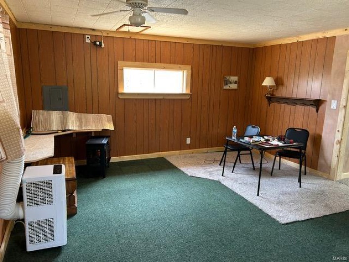 Carpeted home office featuring a ceiling fan, baseboards, and wood walls