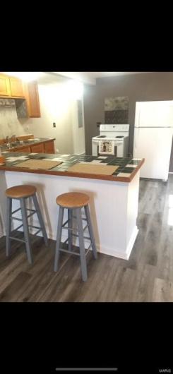 Kitchen featuring kitchen peninsula, dark wood-type flooring, white appliances, and a breakfast bar