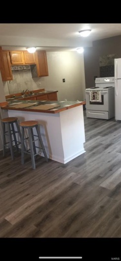 Kitchen with dark / wood-style flooring, kitchen peninsula, a kitchen bar, and white appliances