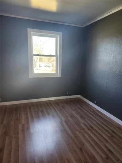 Empty room featuring dark wood-type flooring, ornamental molding, and baseboards