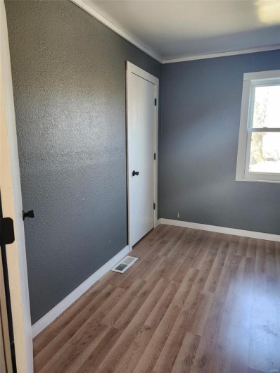 Empty room with baseboards, visible vents, a textured wall, ornamental molding, and wood finished floors