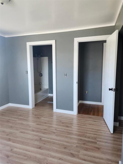 Unfurnished bedroom with baseboards, ornamental molding, ensuite bathroom, and light wood-style floors