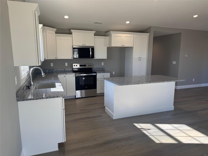 Kitchen featuring sink, appliances with stainless steel finishes, stone countertops, a kitchen island, and white cabinetry