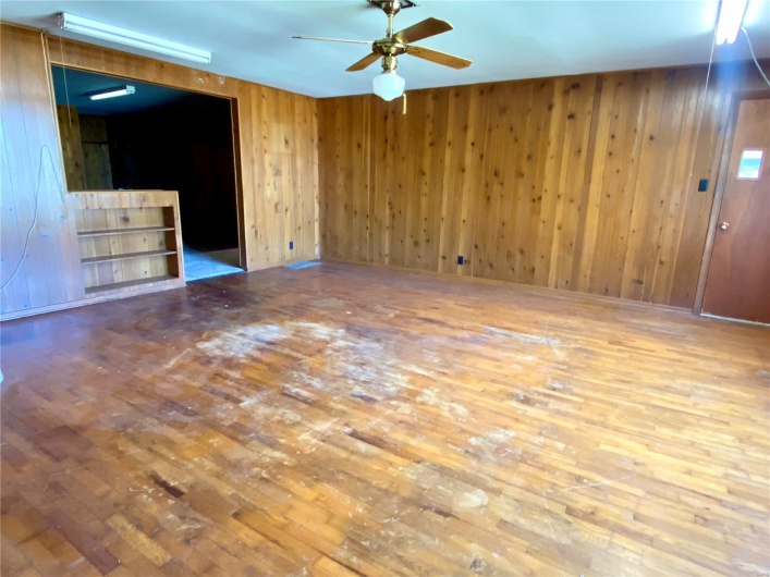 Unfurnished living room with wood-type flooring, ceiling fan, and wooden walls