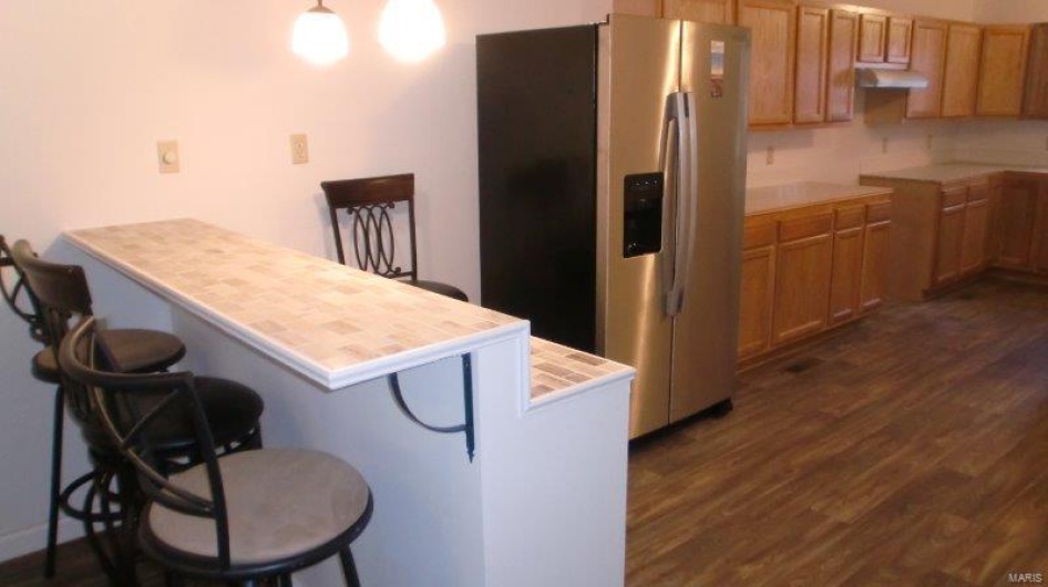 Kitchen with tile counters, stainless steel fridge, a kitchen bar, and dark hardwood / wood-style floors