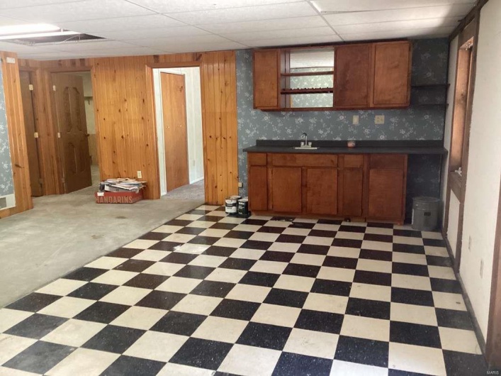 Kitchen featuring a paneled ceiling, wooden walls, and sink