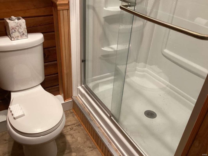 Bathroom featuring walk in shower, wooden walls, and toilet