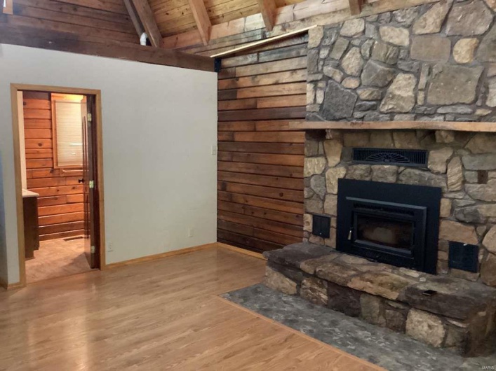 Living room featuring wooden ceiling, a stone fireplace, lofted ceiling with beams, and hardwood / wood-style floors