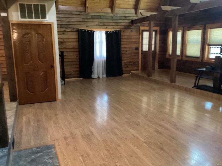 Unfurnished living room with vaulted ceiling with beams, wood-type flooring, wood ceiling, and wood walls