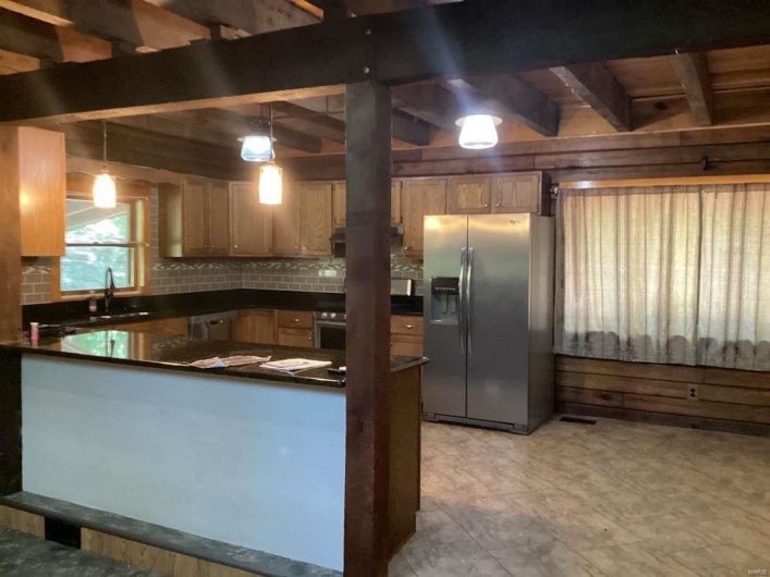 Kitchen with sink, backsplash, hanging light fixtures, and stainless steel fridge