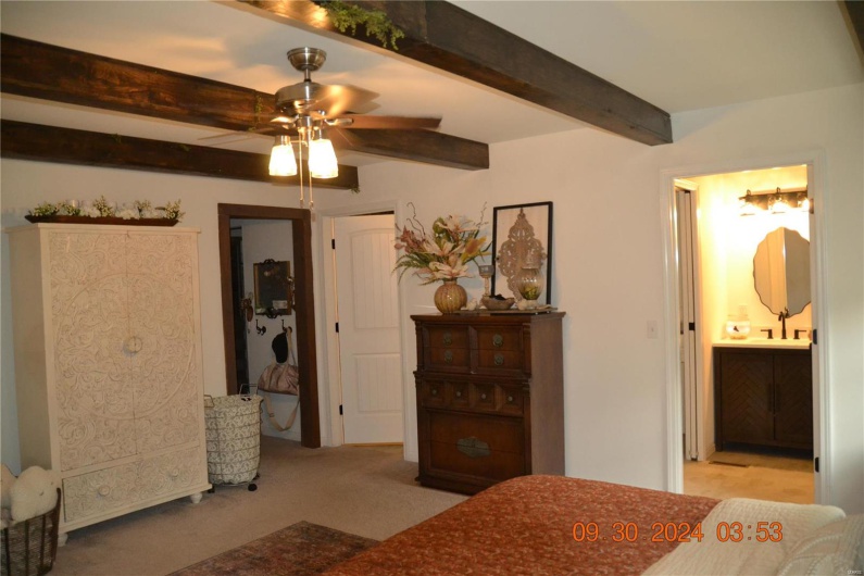 Bedroom with beamed ceiling, sink, light colored carpet, connected bathroom, and ceiling fan
