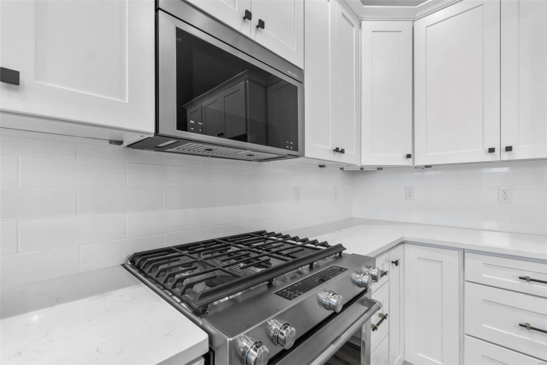 Kitchen with white cabinets, appliances with stainless steel finishes, decorative backsplash, and light stone countertops