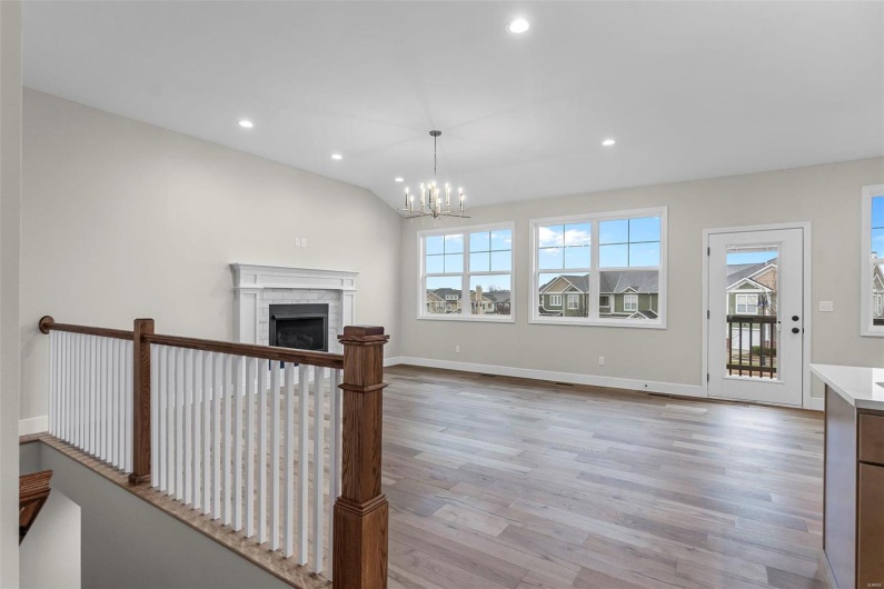 Unfurnished living room featuring vaulted ceiling, light wood-type flooring, a notable chandelier, and a brick fireplace