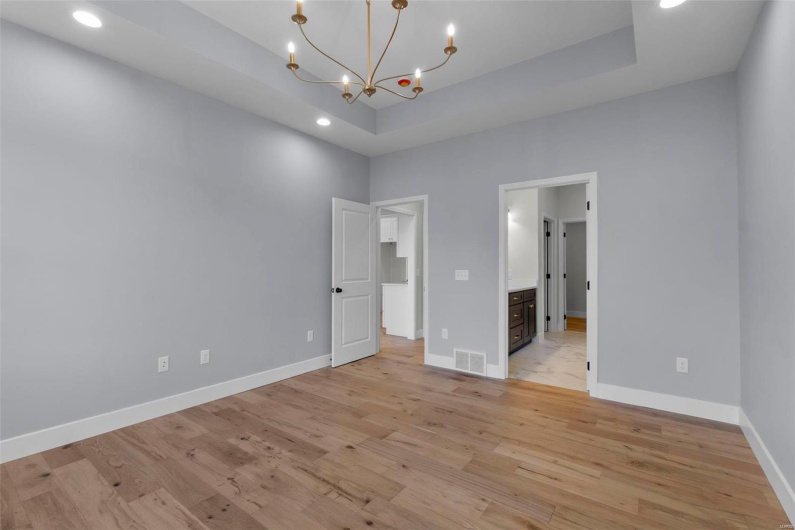 Unfurnished bedroom featuring a tray ceiling, light wood-style flooring, visible vents, and baseboards