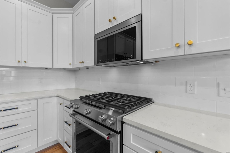 Kitchen with light wood finished floors, white cabinets, light stone counters, appliances with stainless steel finishes, and backsplash