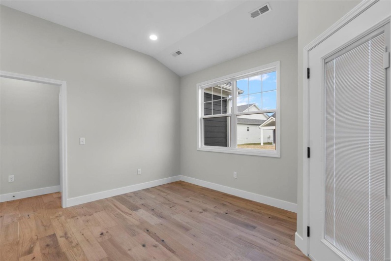 Unfurnished bedroom featuring visible vents, vaulted ceiling, light wood-style flooring, and baseboards