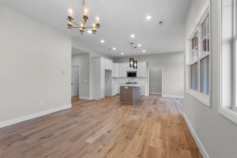 Kitchen featuring stainless steel microwave, baseboards, white cabinets, light wood-style floors, and an island with sink