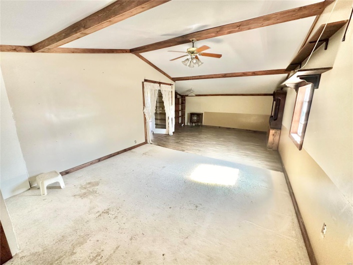Unfurnished living room featuring ceiling fan, vaulted ceiling with beams, and hardwood / wood-style flooring