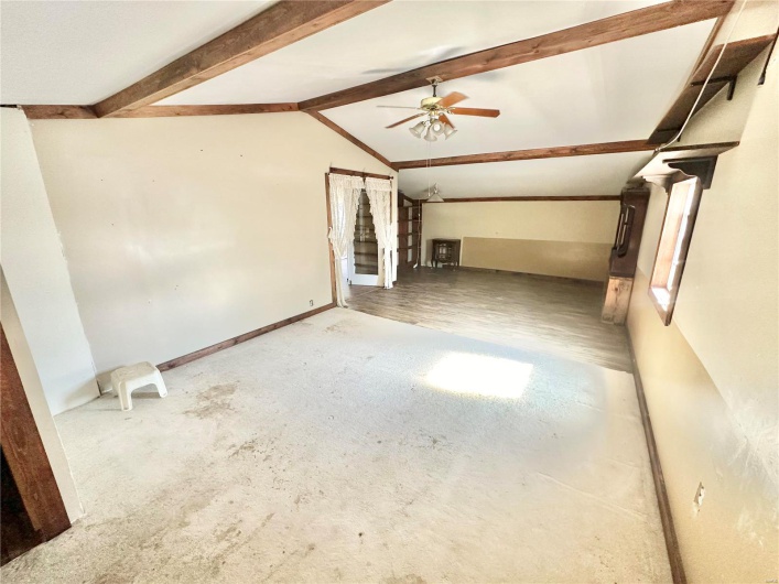Unfurnished living room featuring wood-type flooring, lofted ceiling with beams, and ceiling fan