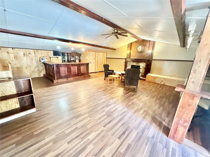 Living area featuring ceiling fan, wood walls, lofted ceiling with beams, a fireplace, and hardwood / wood-style floors