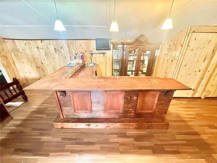 Bar with wooden walls, hanging light fixtures, dark wood-type flooring, and wood counters