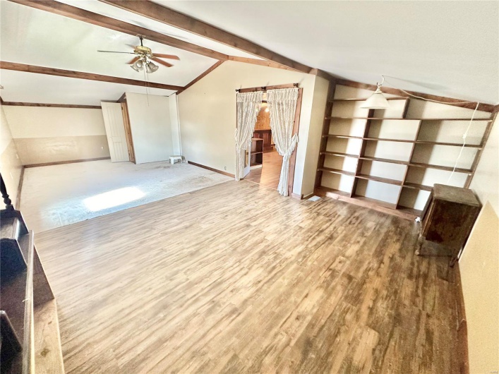Unfurnished living room featuring lofted ceiling with beams, ceiling fan, and wood-type flooring