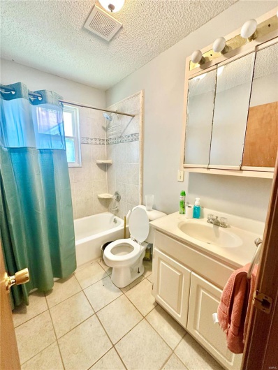 Full bathroom featuring vanity, toilet, a textured ceiling, tile patterned flooring, and shower / tub combo with curtain