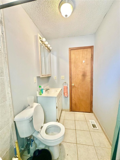 Bathroom featuring vanity, tile patterned flooring, toilet, and a textured ceiling
