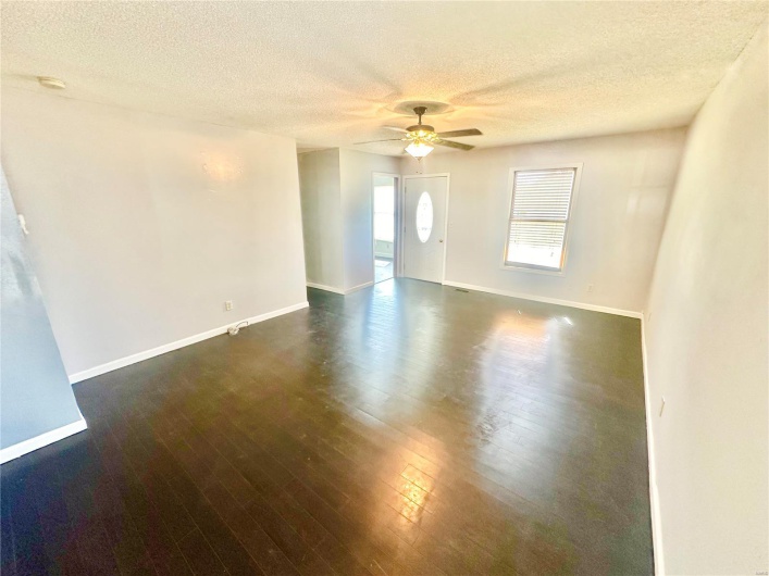 Empty room with ceiling fan, a textured ceiling, and dark wood-type flooring