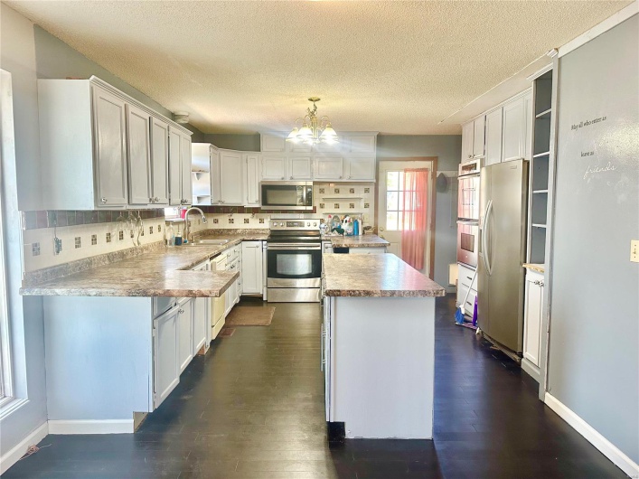 Kitchen featuring white cabinets, tasteful backsplash, decorative light fixtures, appliances with stainless steel finishes, and dark hardwood / wood-style floors