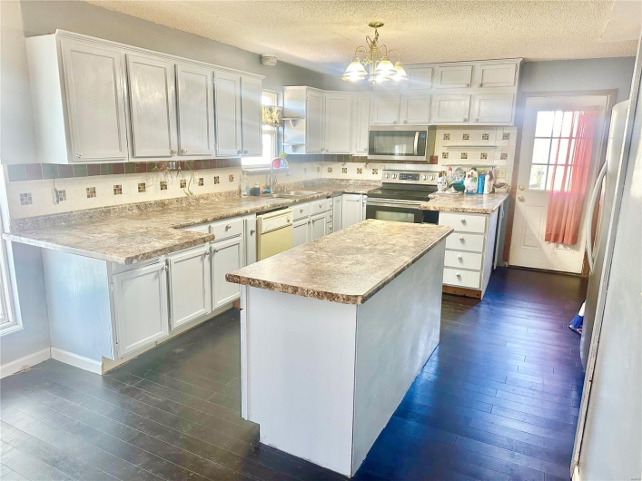 Kitchen featuring stainless steel appliances, tasteful backsplash, decorative light fixtures, and white cabinetry