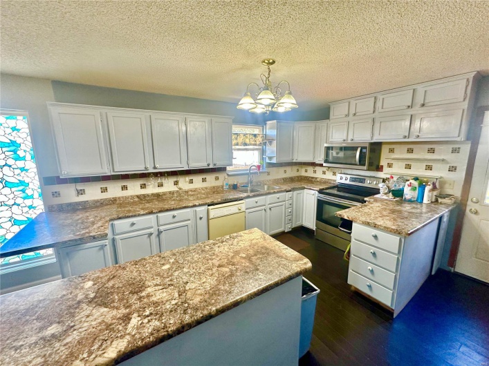 Kitchen with dark hardwood / wood-style flooring, hanging light fixtures, stainless steel appliances, and white cabinets