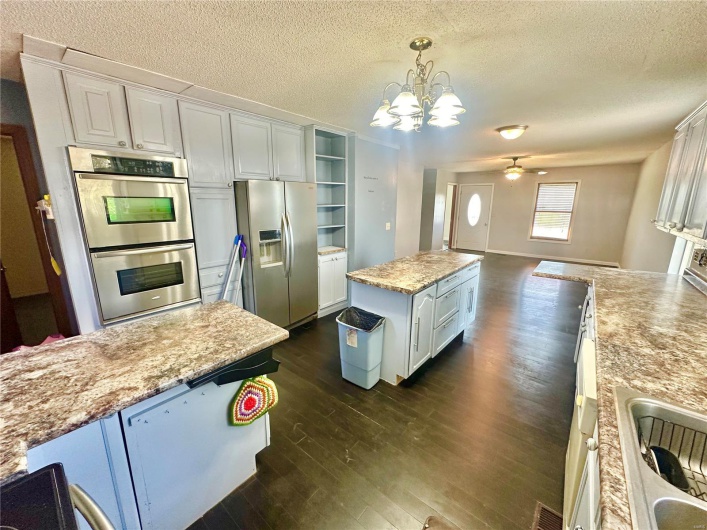 Kitchen with white cabinets, hanging light fixtures, stainless steel appliances, a center island, and dark hardwood / wood-style flooring
