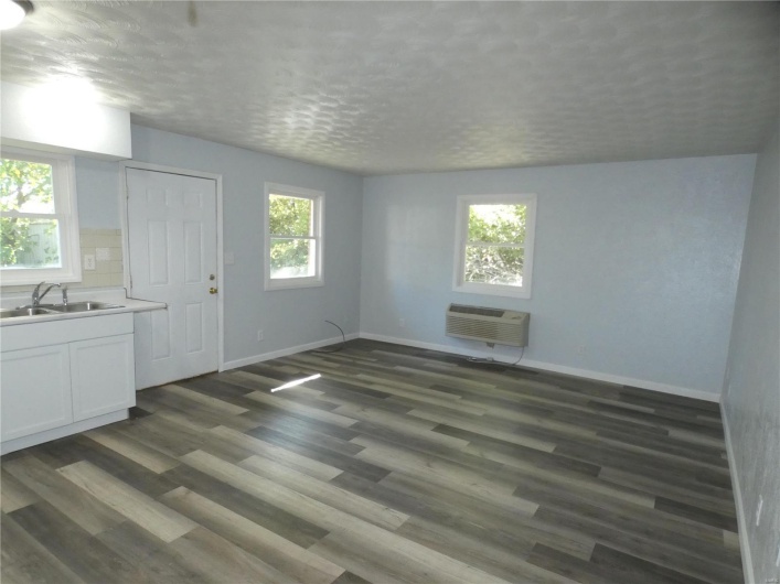 Unfurnished living room with a wall mounted air conditioner, sink, dark hardwood / wood-style floors, and a textured ceiling