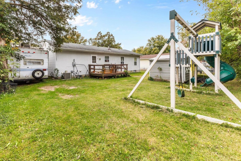 Back of property with cooling unit, a playground, a wooden deck, and a lawn