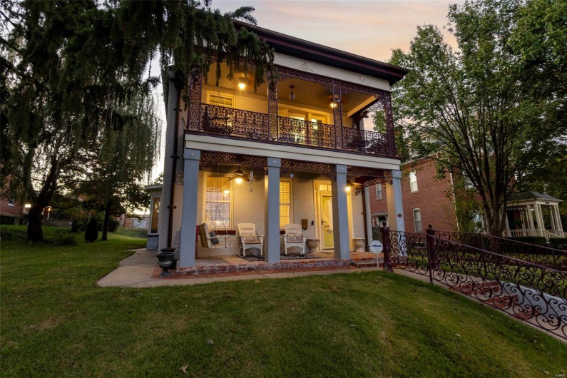 Back house at dusk with a patio area, ceiling fan, a lawn, and a balcony