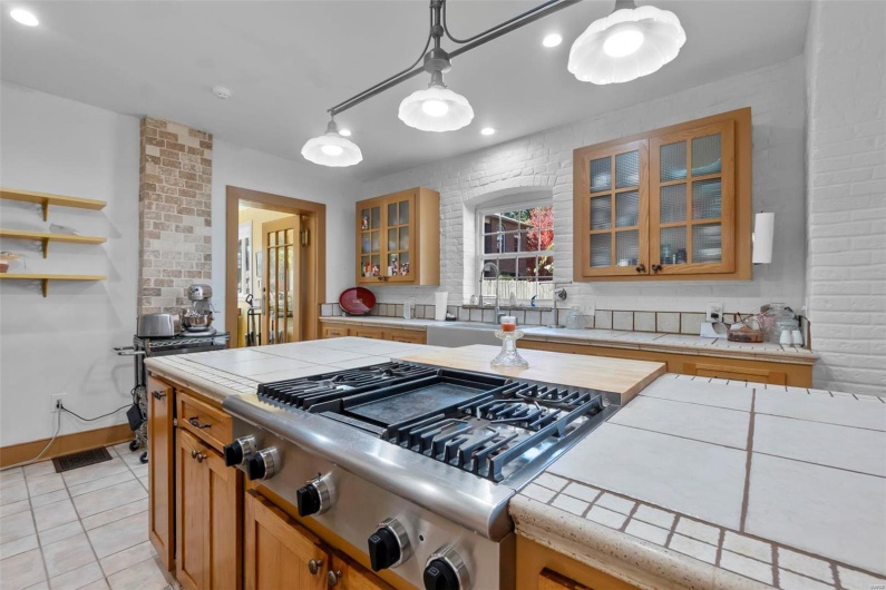 Kitchen with stainless steel gas cooktop, tile counters, sink, pendant lighting, and light tile patterned floors