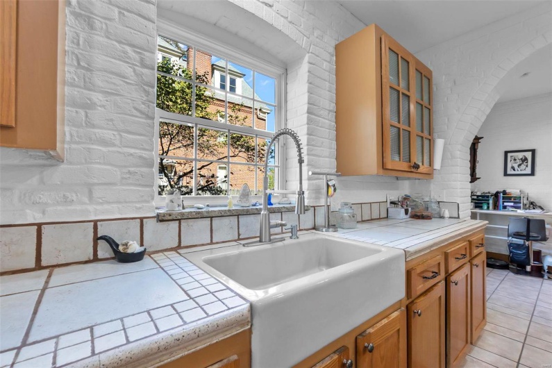 Kitchen with tile countertops, light tile patterned flooring, sink, and brick wall