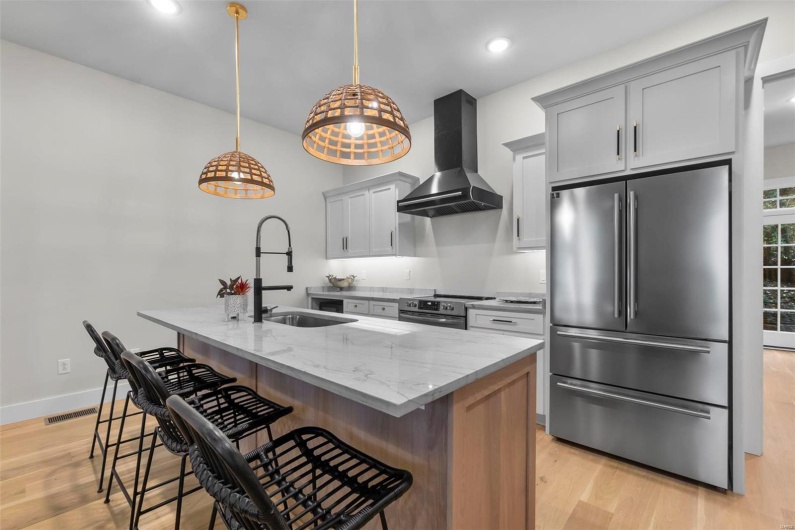 Kitchen with a kitchen bar, stainless steel appliances, wall chimney exhaust hood, light stone counters, and a center island with sink