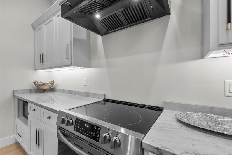 Kitchen with white cabinets, stainless steel range with electric cooktop, light stone countertops, custom range hood, and light hardwood / wood-style floors