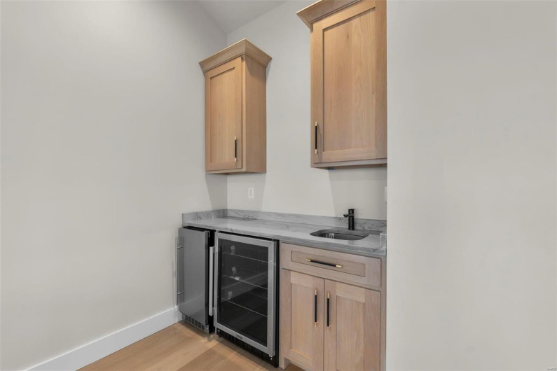Bar with light brown cabinets, light hardwood / wood-style flooring, wine cooler, stainless steel fridge, and sink