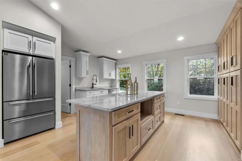 Kitchen featuring a kitchen island, white cabinetry, light brown cabinetry, light wood-type flooring, and stainless steel appliances