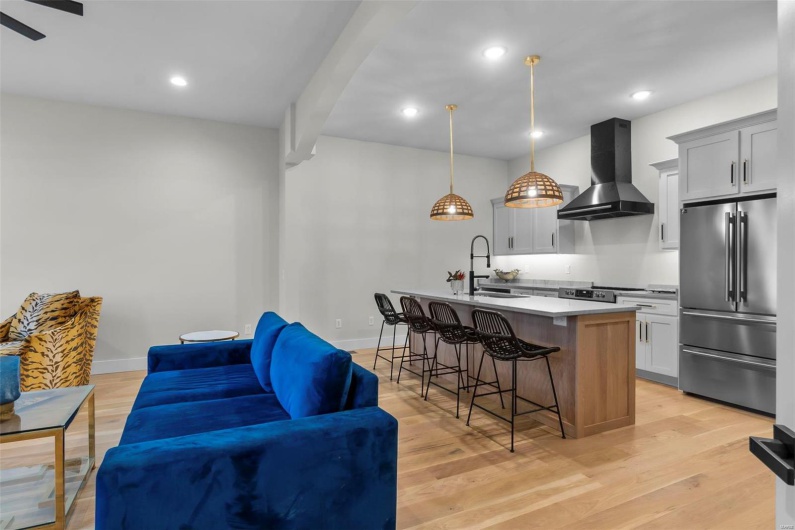 Kitchen featuring a kitchen island with sink, wall chimney range hood, high end fridge, sink, and decorative light fixtures