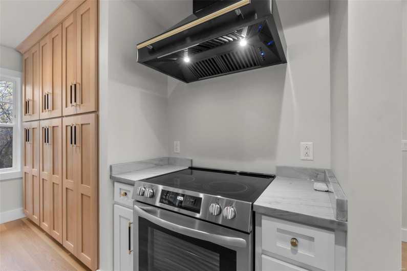 Kitchen with light stone countertops, wall chimney range hood, stainless steel range with electric stovetop, light hardwood / wood-style flooring, and light brown cabinets
