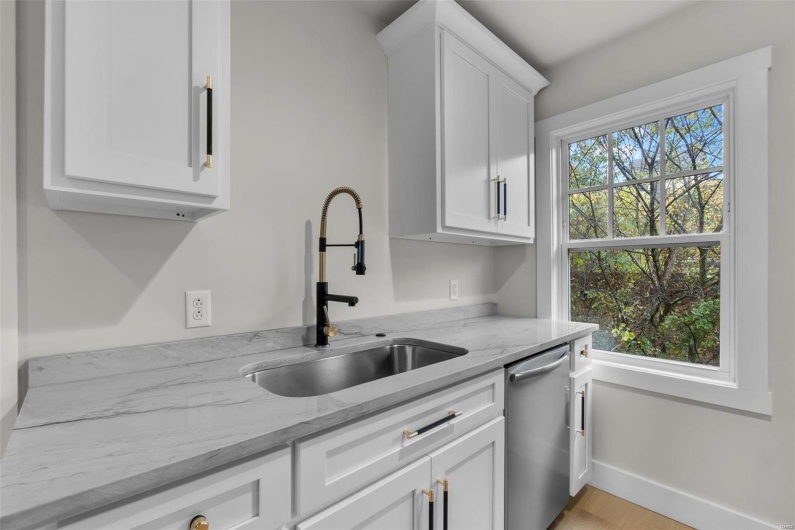 Kitchen with sink, dishwasher, white cabinets, and light stone counters