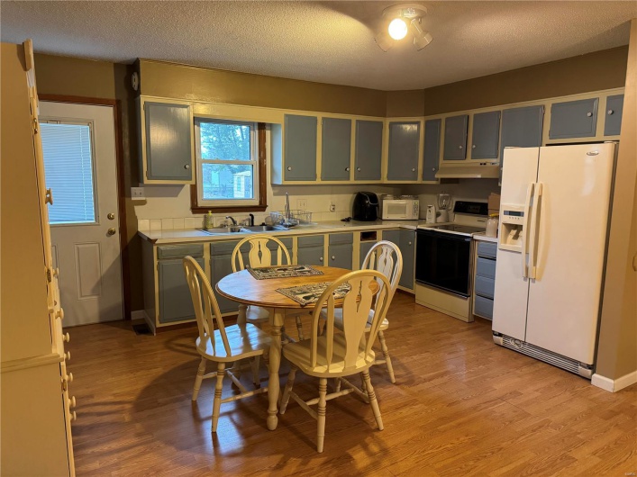 Kitchen with sink, a textured ceiling, white appliances, ventilation hood, and light hardwood / wood-style flooring
