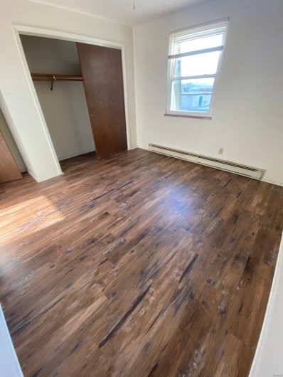 Unfurnished bedroom with a closet, dark wood-type flooring, and a baseboard radiator