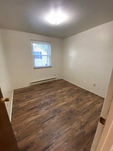Unfurnished room featuring dark hardwood / wood-style floors and baseboard heating
