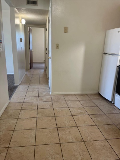 Hallway with light tile patterned flooring and a textured ceiling