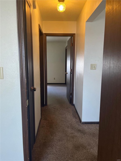 Corridor featuring a textured ceiling and dark carpet